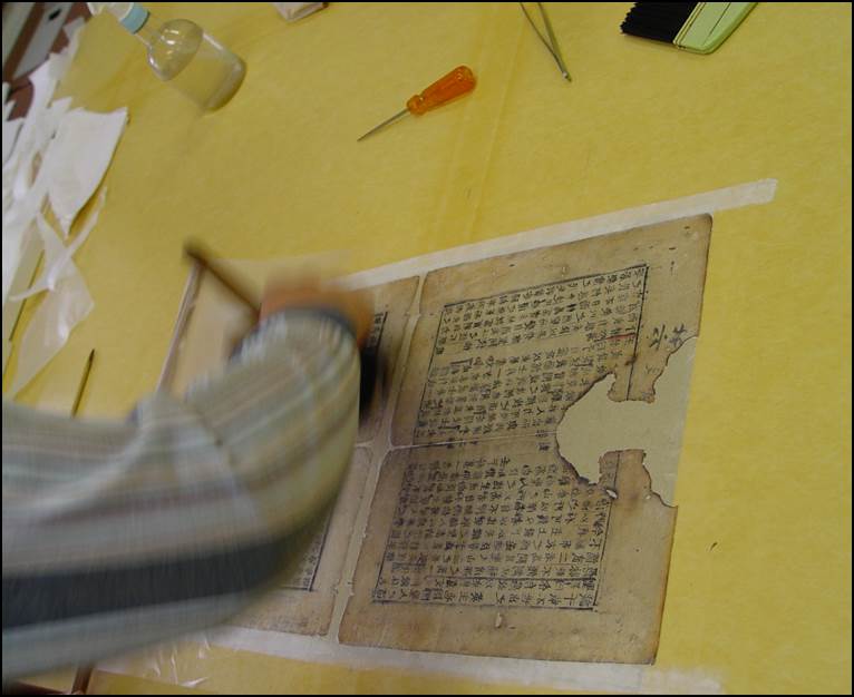 들대를 이용하여 풀칠한 배접지를 책지 위에 씌우고 문지름솔로 문질러주는 작업